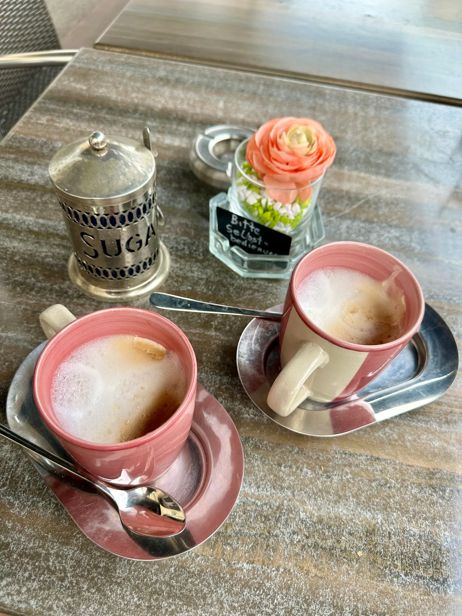 Zwei Kaffees, Zuckerdose und eine Blume auf dem Terrassentisch